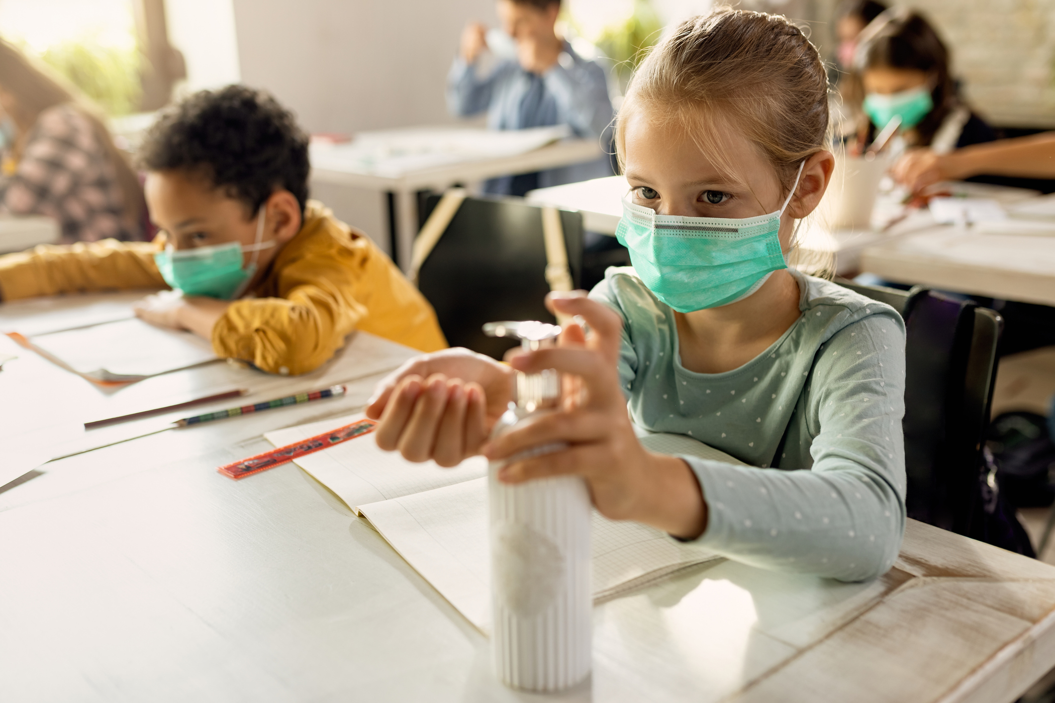Foto em close de uma menina e um menino sentados à mesa, em uma sala de aula