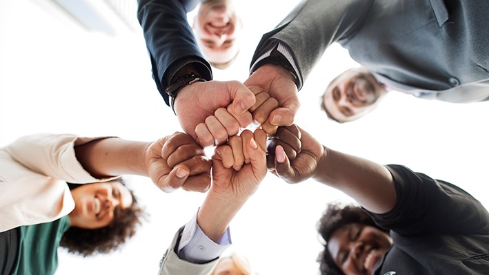 Cinco pessoas unem as mãos com os punhos cerrados