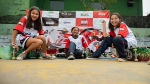 Meninas beneficiárias do projeto Social Skate posam para foto em frente a banner institucional de iniciativa apoiada pelo Instituto Neoenergia