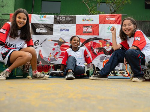 Meninas beneficiárias do projeto Social Skate posam para foto em frente a banner institucional de iniciativa apoiada pelo Instituto Neoenergia
